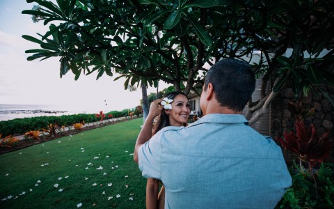 a man putting a white hawaiian flower in a womans hair