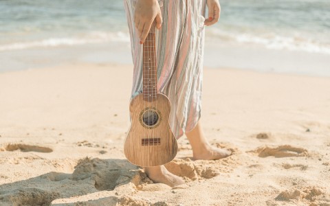 woman holding a ukelele while standing on the beach