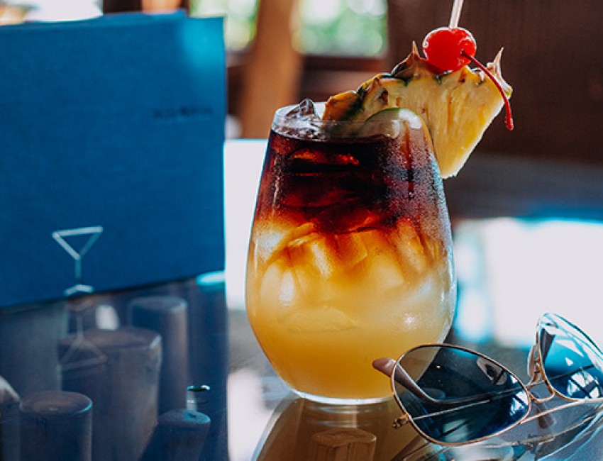 a tropical cocktail with a cherry and a slice of pineapple on top next to a pair of sunglasses