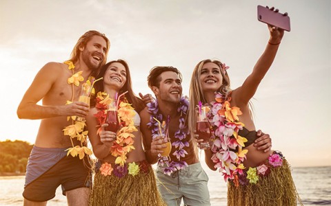 two couples with leis and drinks taking a selfie by the ocean