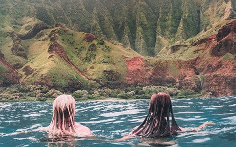 two girls swimming in the ocean and looking at the large mountains