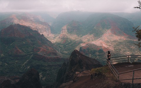 view of the large mountain range on a cloudy day and a woman viewing from an overlook