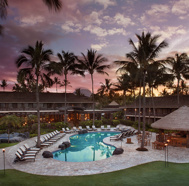 view of the hotel pool area with several pool chairs and a tiki hut