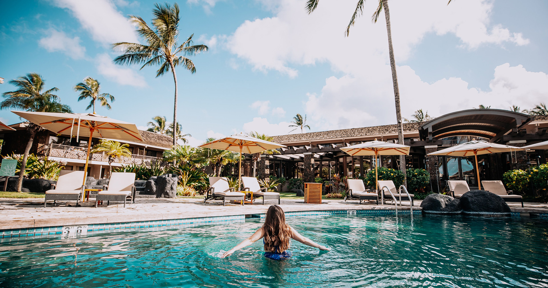 Woman swimming in the pool surrounded by daybeds and umbrellas