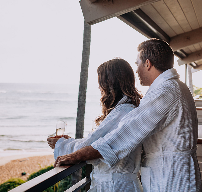 a couple standing on the balcony with a glass of champagne looking at the ocean