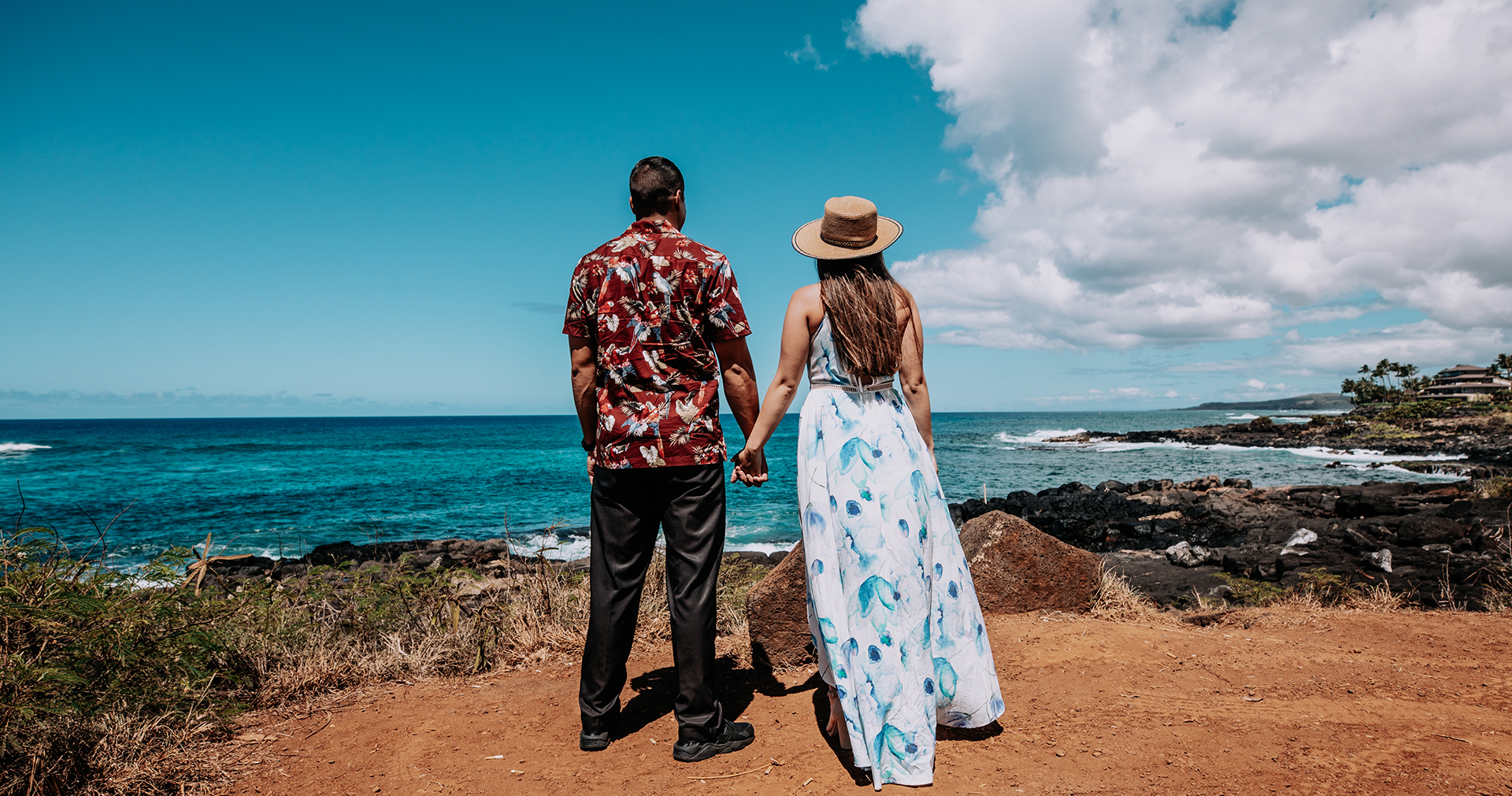 man and woman holding hands and looking at the ocean from the mountains