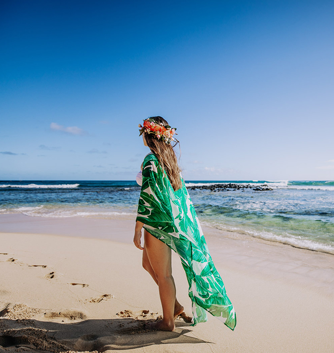 woman with a green hawaiian shaw and a lei standing on the beach