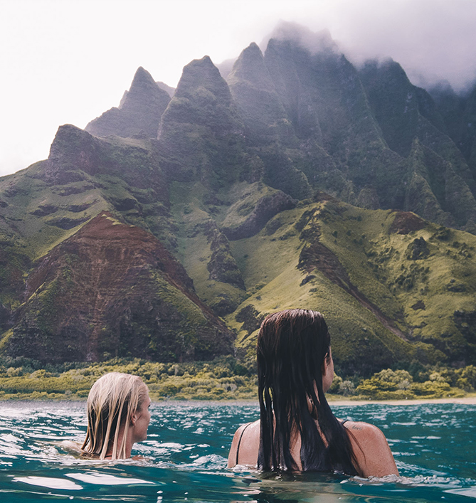 two girls in the ocean looking at the mountains