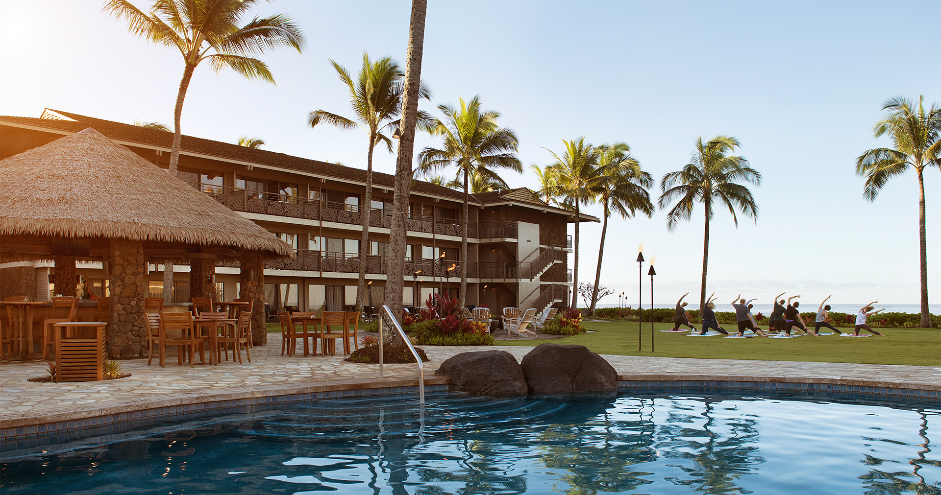 view of the hotel and the hotel pool with a group of people doing yoga on the lanai