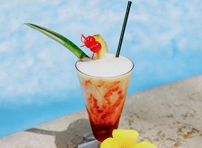 view of a tropical cocktail with a pineapple and a cherry next to the pool