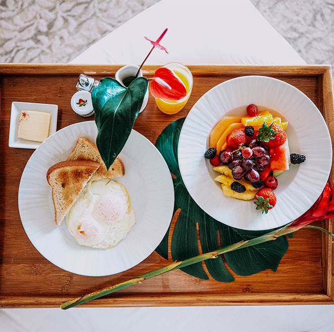 overhead view of a breakfast meal with toast, eggs, fruit, and orange juice served on a wooden tray