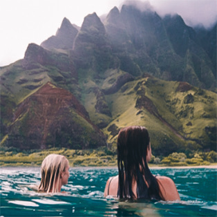 Two women in the ocean looking at cliffs