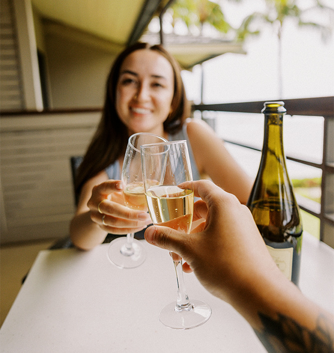 a couple clinking their glasses of champagne while sitting on their balcony