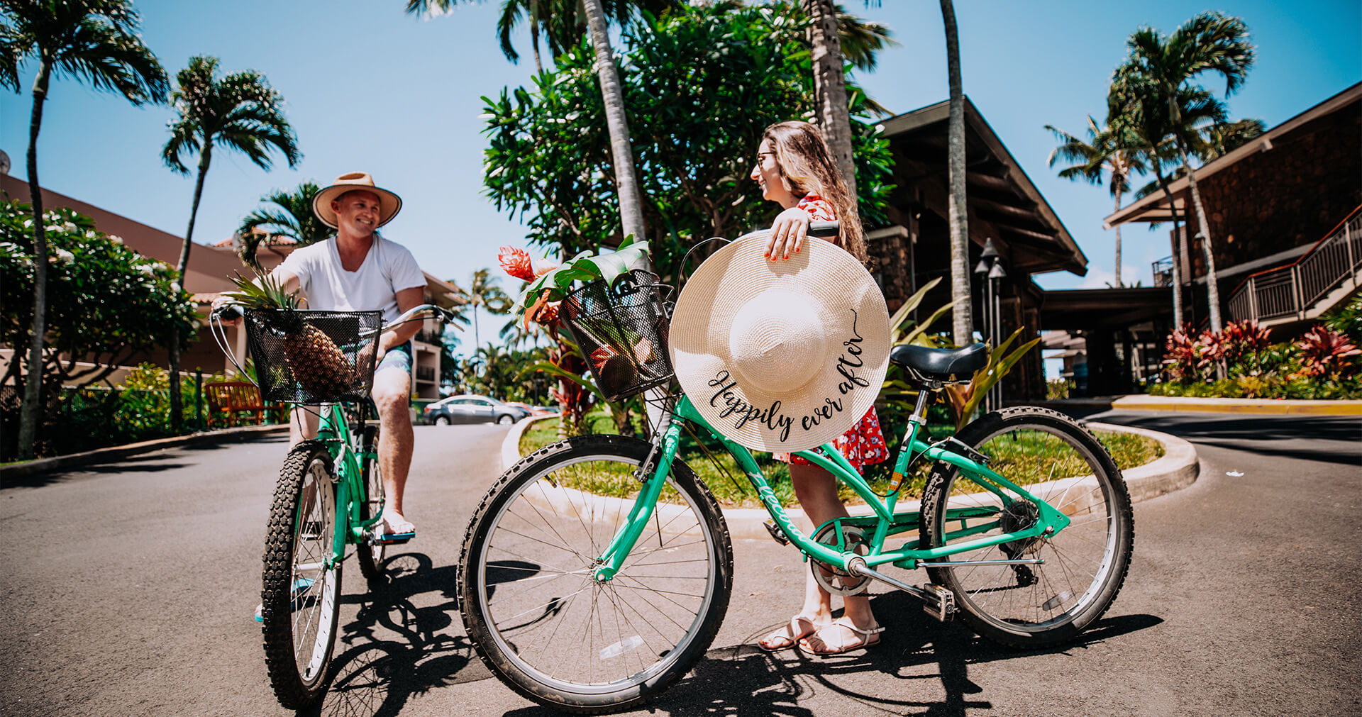 man riding a bicycle next to a woman with a bike holding a hat that says happily ever after