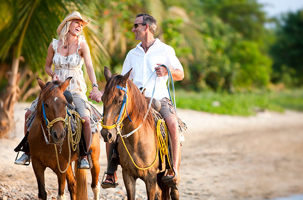 a couple holding hands and laughing while horseback riding on the beach