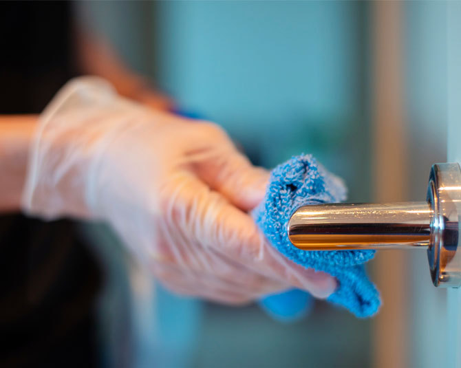 hand wiping door handle with cloth with gloves