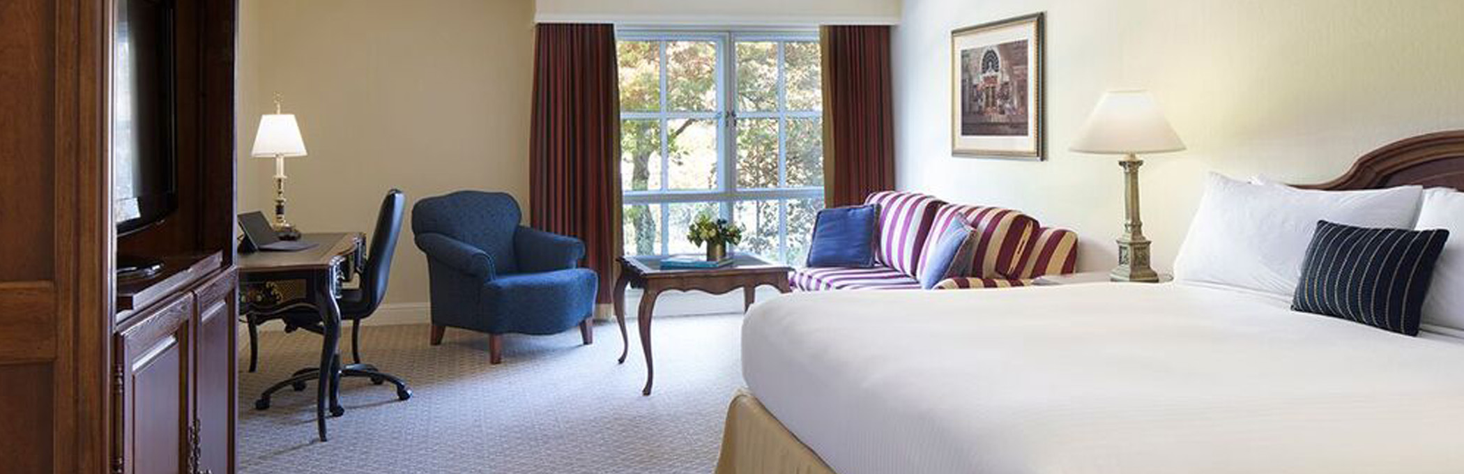 white bed across from a dark wood cabinet, blue chair and brown desk in the corner