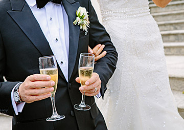 a man in a suit holding two drinks in his hand next to a bride