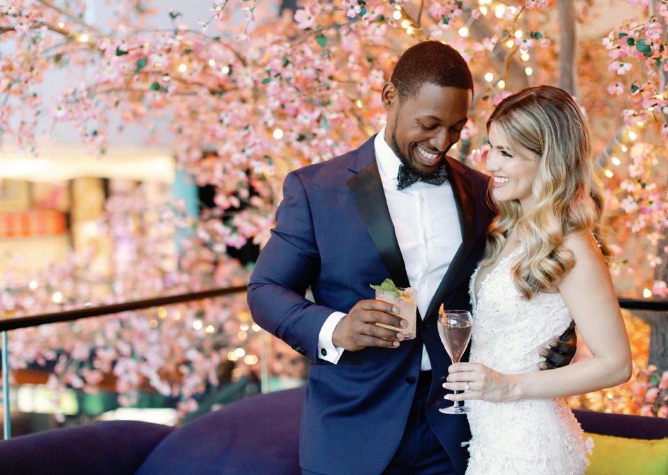 bride and groom holding cocktails in front of pink flower tree