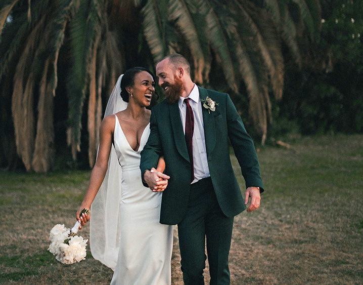 wedding couple walking and laughing with a palm tree behind them 