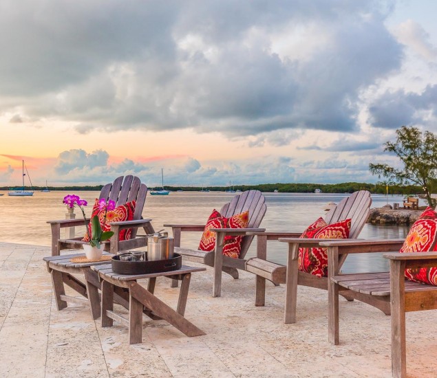 4 patio chairs with red accent pillows all on the sand while sun sets