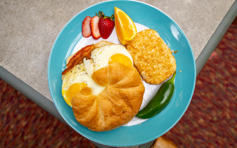top view of a croissant sandwich with eggs, a strawberry, a slice of orange and a hash-brown 