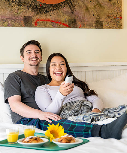 a smiling man and woman laying in a bed with breakfast next to them
