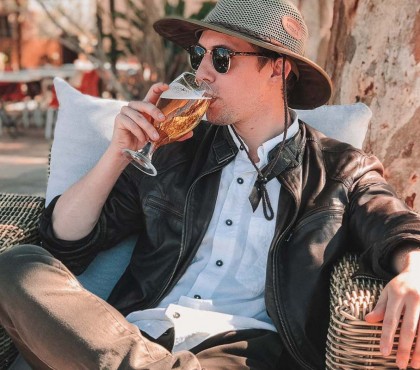 A man wearing a hat and sunglasses having a beer