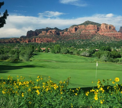 View of a large golf field, some yellow flowers and a rocky mountain in the background