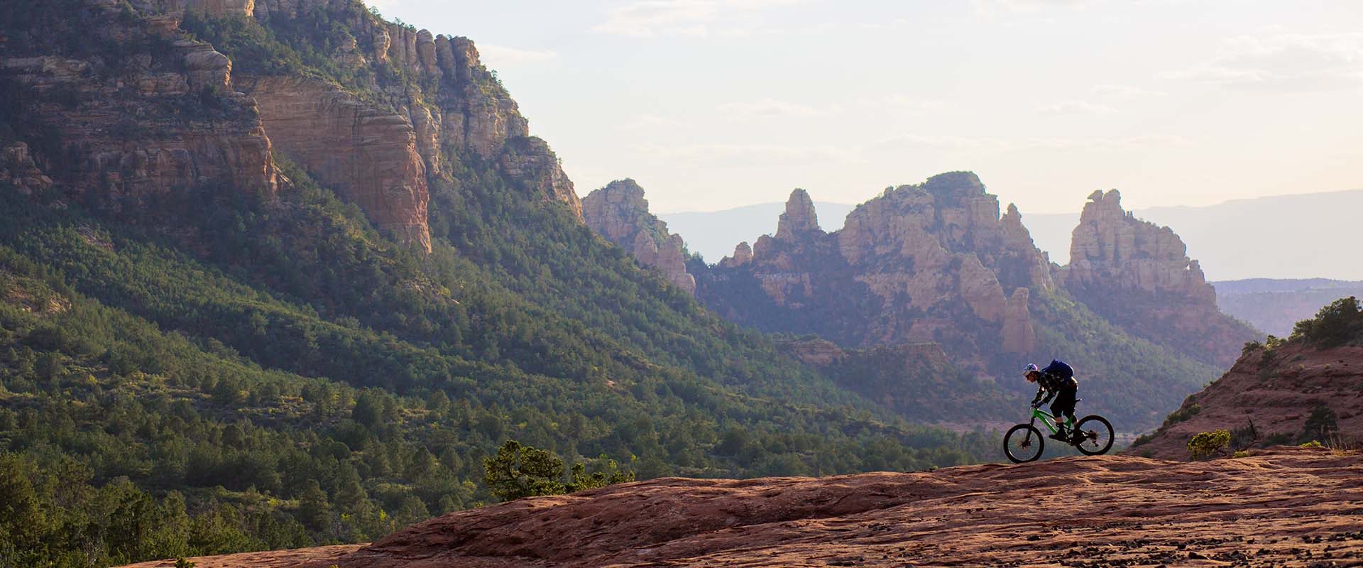 View of a person riding a bike on a rocky road with large rocky mountains as a background