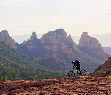 View of a person riding a bike on a rocky road with large rocky mountains as a background