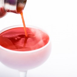 close up of a red cocktail being poured into a chilled glass