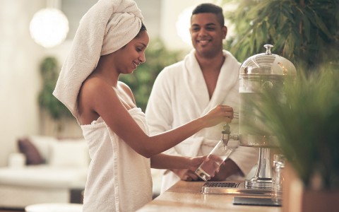 a couple dressed in towels and robes getting a glass of water