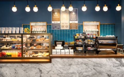 Marble coffee counter with pastry case and assorted snack offerings in front of blue-tiled wall