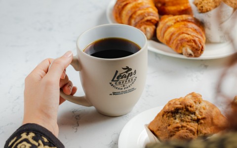 Woman holding cup of coffee in a Leaps coffee mug surrounded by plated pastries