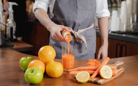 Barista pouring carrot juice into a glass surrounded by lemons and carrots