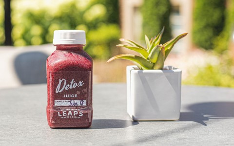 detox red juice bottle next to a plant in a pot on a table outside