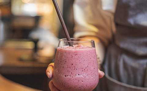 red smoothie in a glass with a straw being held by a server