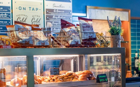 glass case with a bunch of pastries and chips on top with menu on the background wall