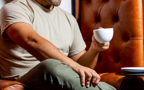 man enjoying and looking down at his coffee while sitting on a couch
