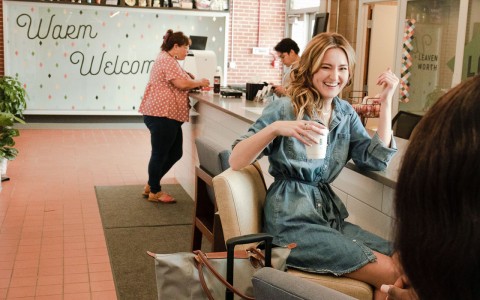 woman sitting in a chair and laughing while holding a cup 