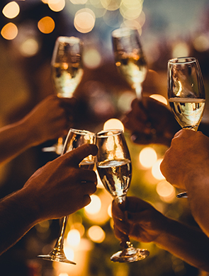 people holding champagne glasses with fairy lights behind them