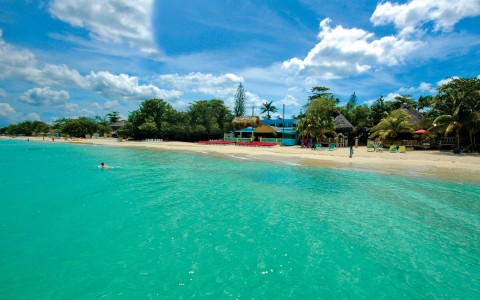 view of Legends Resort beach area from the clear turquoise water with a man swimming in the calm waters