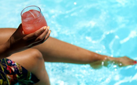 young woman splashing her feet in the pool while enjoying a refreshing cocktail