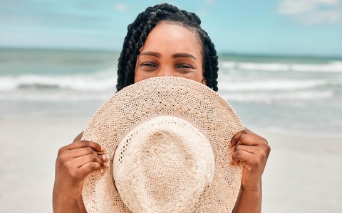 playful and happy young woman peaking over a sunhat hiding her smile