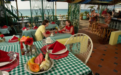 couple dining at casual beachfront restaurant and bar with other guests relaxing at the bar