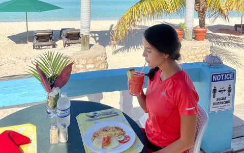 athletic young woman sipping fresh juice at breakfast at an open air dining location on the beach