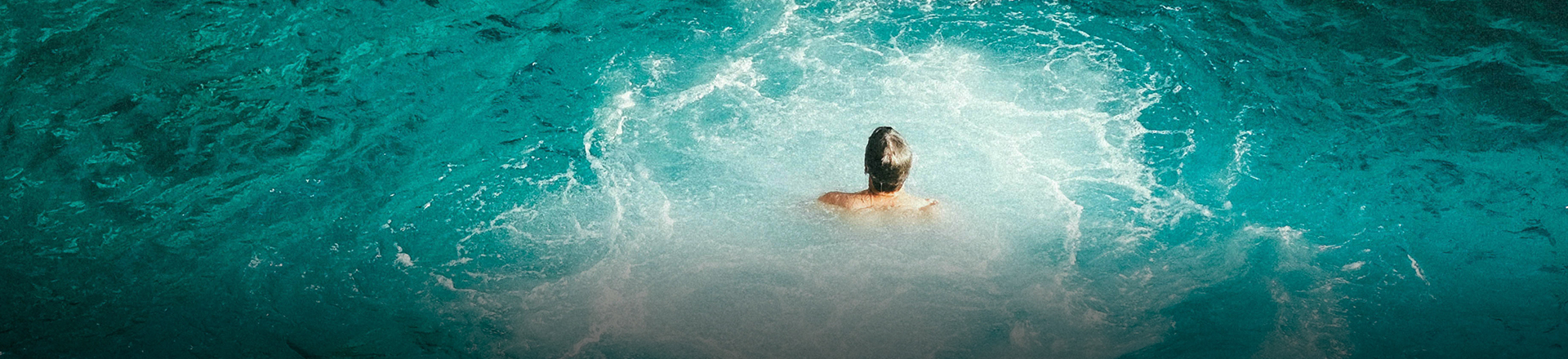 man swimming in crystal blue water with gentle white crash waves
