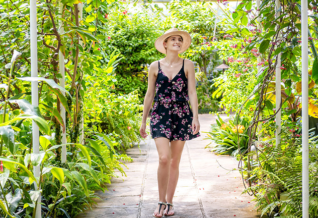young woman in sundress casually taking a walk along a cobblestone path in a tropical garden