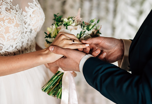close up of formally dressed bride and groom, groom sliding wedding ring onto brides finger